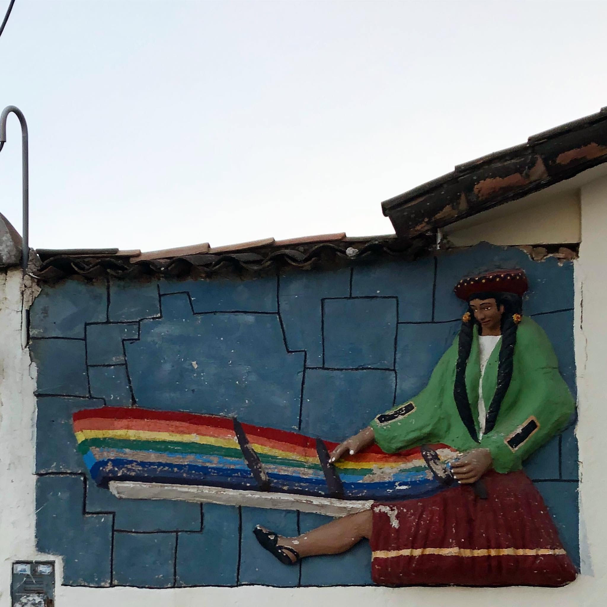 A sculpted facade of a woman weaving a rainbow pattern